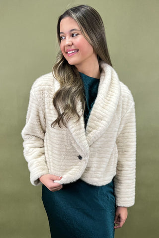 Woman wearing a cream knitted cardigan against a green background