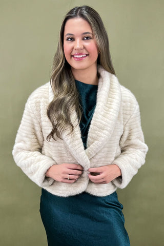 Woman wearing a cream-colored knitted cardigan against a green background