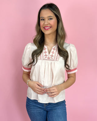 Woman wearing a white blouse with red embroidery against a pink background