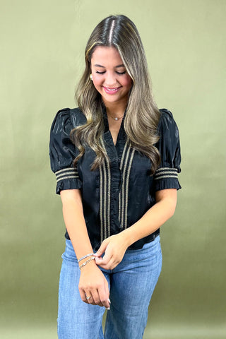 Woman wearing a black blouse with puff sleeves and blue jeans against a green background