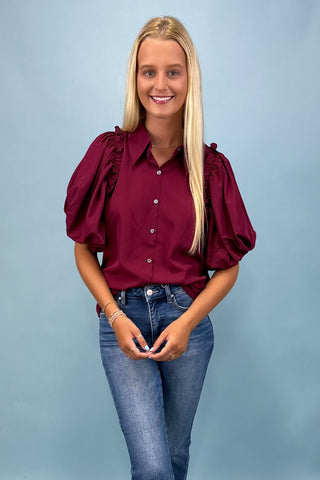 Woman wearing a burgundy blouse with puff sleeves and blue jeans against a light blue background