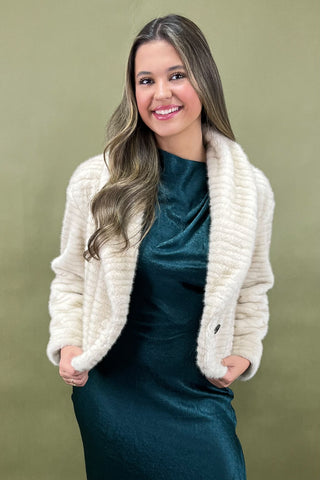 Woman wearing a white fur shrug over a teal dress against a green background