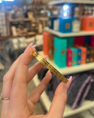 Weisinger Designs Hail Mary Gold Bangle Bracelet. Clasp Open and Close Bracelet, Adult Size displayed in a store background. 