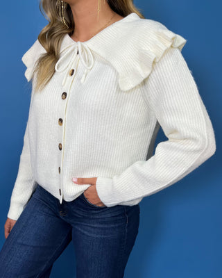 Ivory ribbed knit cardigan with long sleeves, button front, oversized ruffle collar and tie neckline.
