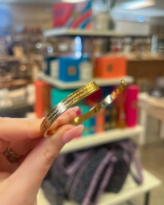 Weisinger Designs Hail Mary Gold Bangle Bracelet. Clasp Open and Close Bracelet, Adult Size displayed in a store background. 