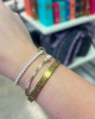 Weisinger Designs Hail Mary Gold Bangle Bracelet. Clasp Open and Close Bracelet, Adult Size displayed in a store background. 