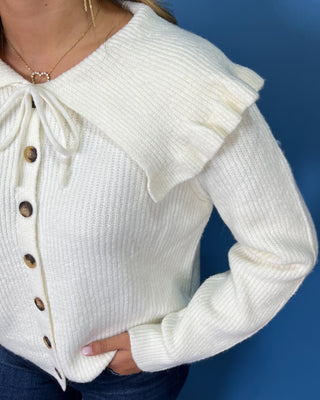 Ivory ribbed knit cardigan with long sleeves, button front, oversized ruffle collar and tie neckline.