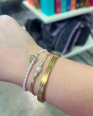 Weisinger Designs Hail Mary Gold Bangle Bracelet. Clasp Open and Close Bracelet, Adult Size displayed in a store background. 