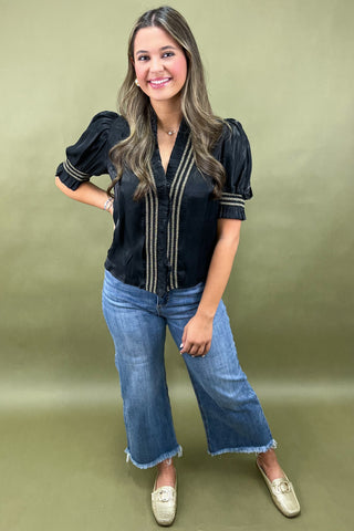 Woman wearing a black blouse with puff sleeves and blue jeans on a green background