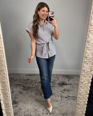 Woman taking a mirror selfie wearing a striped shirt and jeans in a room with a decorative mirror.