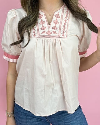 White blouse with red embroidery on a pink background