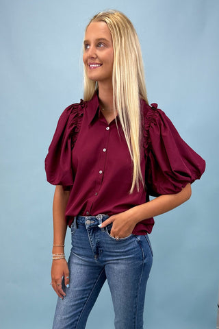 Woman wearing a burgundy blouse with puff sleeves and blue jeans against a light blue background