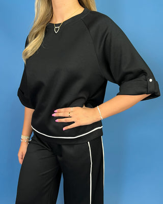 A woman wearing a black short-sleeve top with white piping and matching black pants with a white side stripe