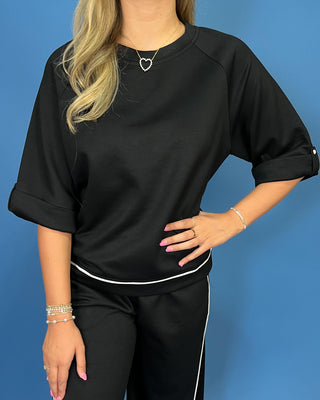 A woman wearing a black short-sleeve top with white contrast piping and matching black pants with white side piping