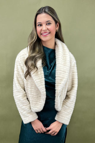 Woman wearing a cream-colored cardigan over a teal top against a green background
