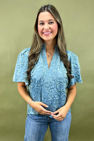 Woman wearing a blue textured blouse and jeans against a green background