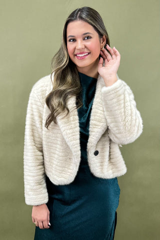 Woman wearing a cream knitted jacket against a green background