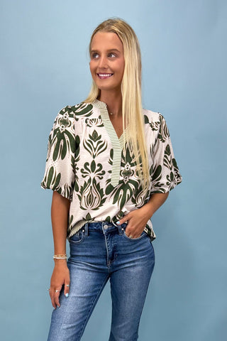 Woman wearing a patterned blouse and jeans against a blue background