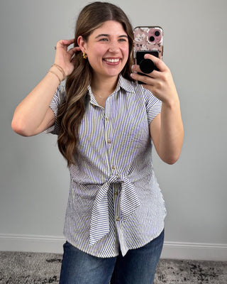 Woman taking a mirror selfie wearing a striped shirt and jeans against a gray wall.