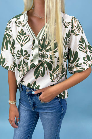 Person wearing a green and white patterned blouse with blue jeans against a light blue background