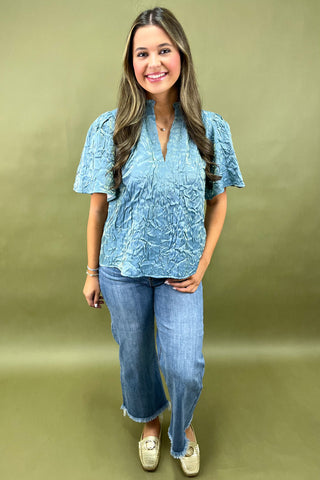 Woman wearing a blue textured blouse and jeans against a green background