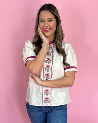 Woman wearing a white blouse with floral embroidery on a pink background