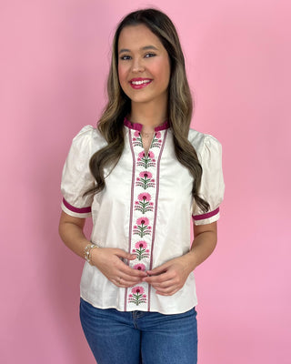 Woman wearing a white blouse with pink floral embroidery against a pink background