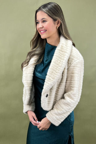 Woman wearing a cream knitted jacket against a green background