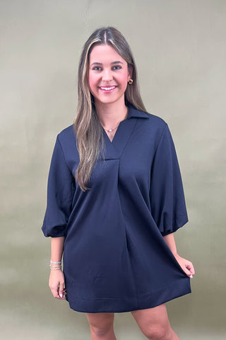 Woman wearing a navy blue dress against a plain background
