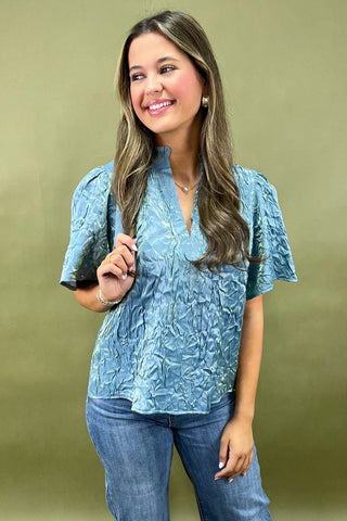 Woman wearing a blue patterned blouse and jeans against a green background