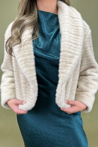 Person wearing a textured white cardigan over a teal dress against a green background