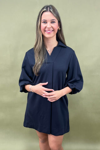 Woman wearing a navy blue dress against a green background