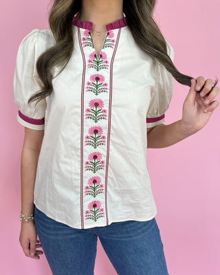 White blouse with pink floral embroidery on a pink background