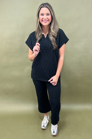 Woman wearing a black outfit with silver shoes against a green background
