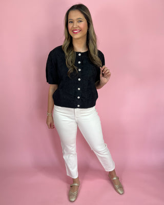 Woman wearing a black button-up top and white pants against a pink background