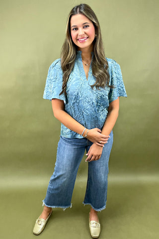 Woman wearing a blue lace top and jeans against a green background