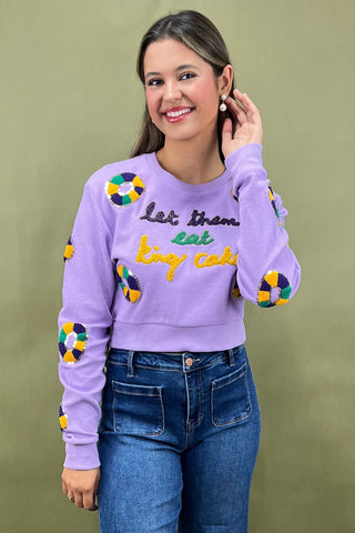 Woman wearing a purple sweatshirt with colorful designs and text, standing against a green background