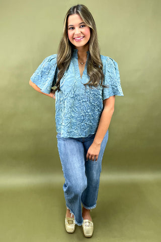 Woman wearing a blue patterned blouse and jeans on a green background