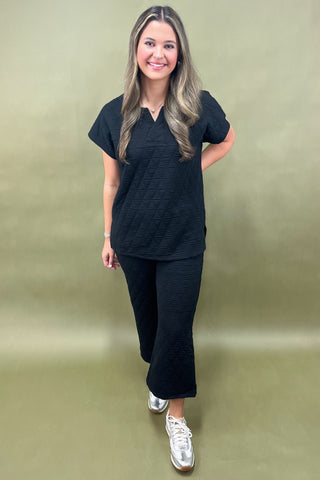 Woman wearing a black outfit standing against a plain background