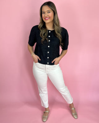Woman wearing a black button-up shirt and white pants against a pink background