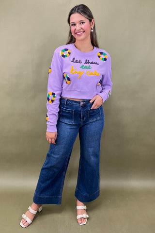 Woman wearing a purple sweatshirt with colorful text and blue jeans on a beige background