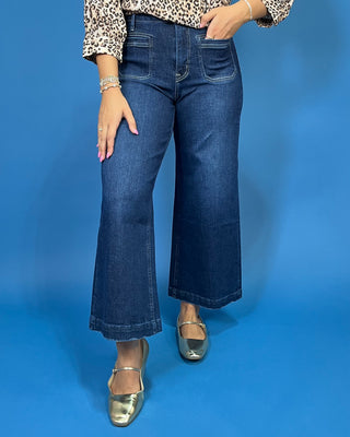 A person wearing dark blue cropped flare jeans with a leopard-print top and metallic silver shoes