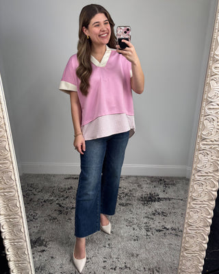 Woman taking a mirror selfie wearing a pink top and blue jeans.