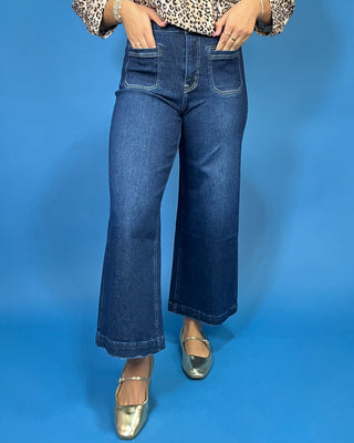 A person wearing dark blue wide-leg cropped jeans with front patch pockets, paired with a leopard-print top and metallic silver flats