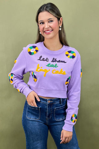 Woman wearing a purple sweatshirt with colorful designs and text, standing against a green background