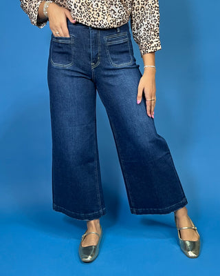 A person wearing dark blue wide-leg cropped denim jeans, a leopard print top, and metallic silver flats
