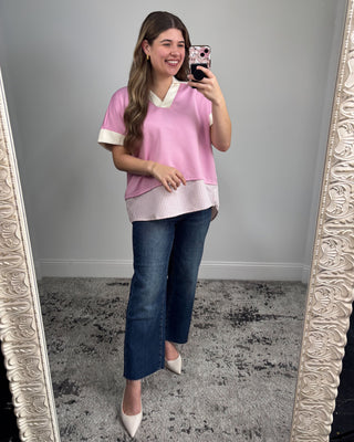 Woman taking a mirror selfie wearing a pink top and blue jeans.