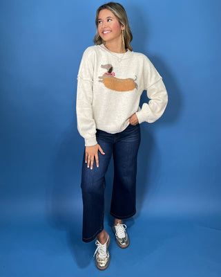 Ivory knit sweater with long sleeves, relaxed fit and a playful dachshund hot dog graphic.