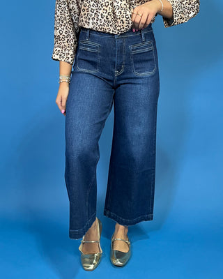 A person wearing dark blue wide-leg cropped jeans, a leopard-print blouse, and metallic gold flats