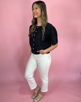 Woman wearing a black top and white pants on a pink background